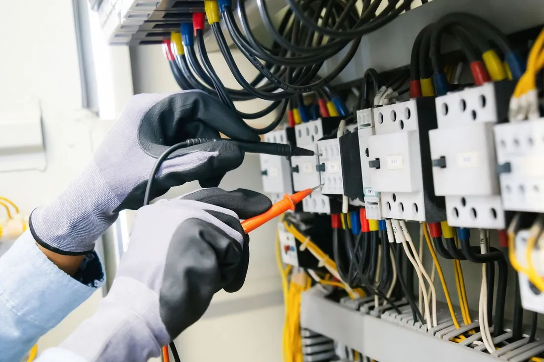 Elektryk w rękawicach mierzy napięcie w rozdzielnicy z zabezpieczeniami